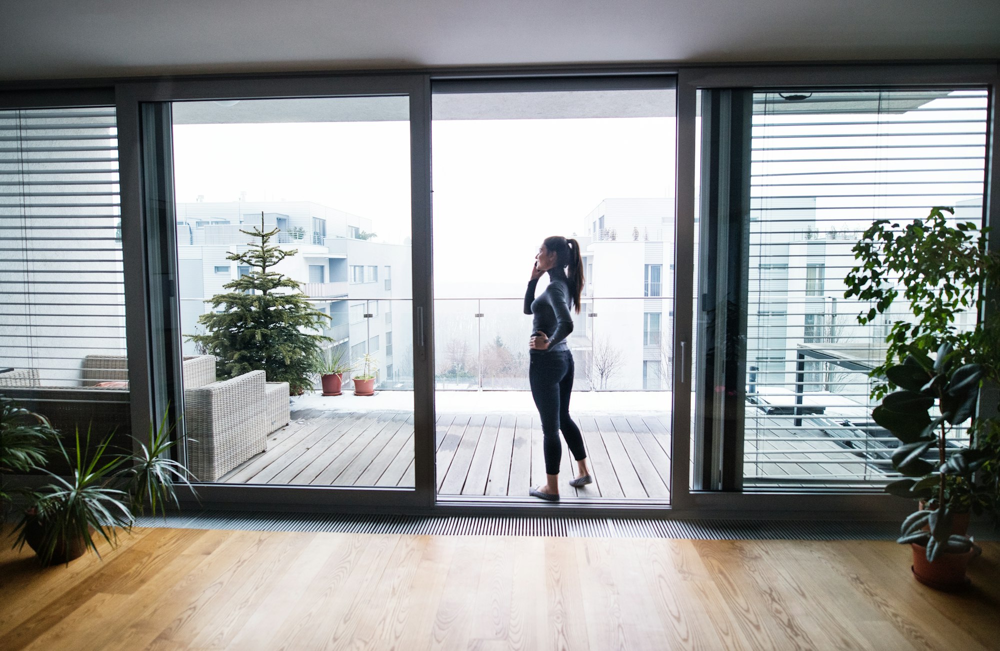 Woman by the window with smartphone, making a phone call.